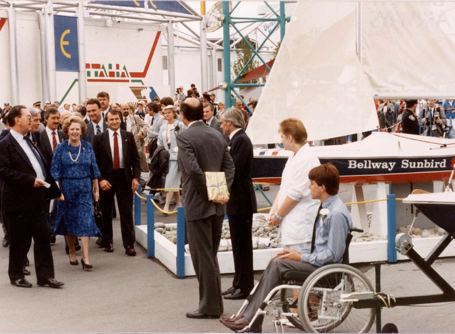 A group of people standing in front of a Sunbird sailboat. Sam Sullivan in wheelchair in foreground.