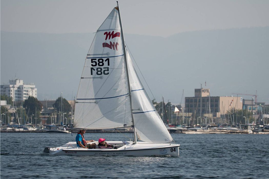 Martin 16 sailboat on the water with two people onboard, city of Kelowna in background