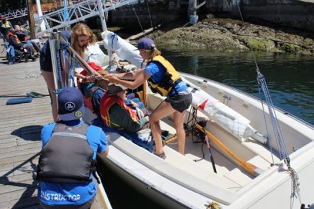 Three people transferring a sailor into a Sonar sailboat using a hydraulic lift