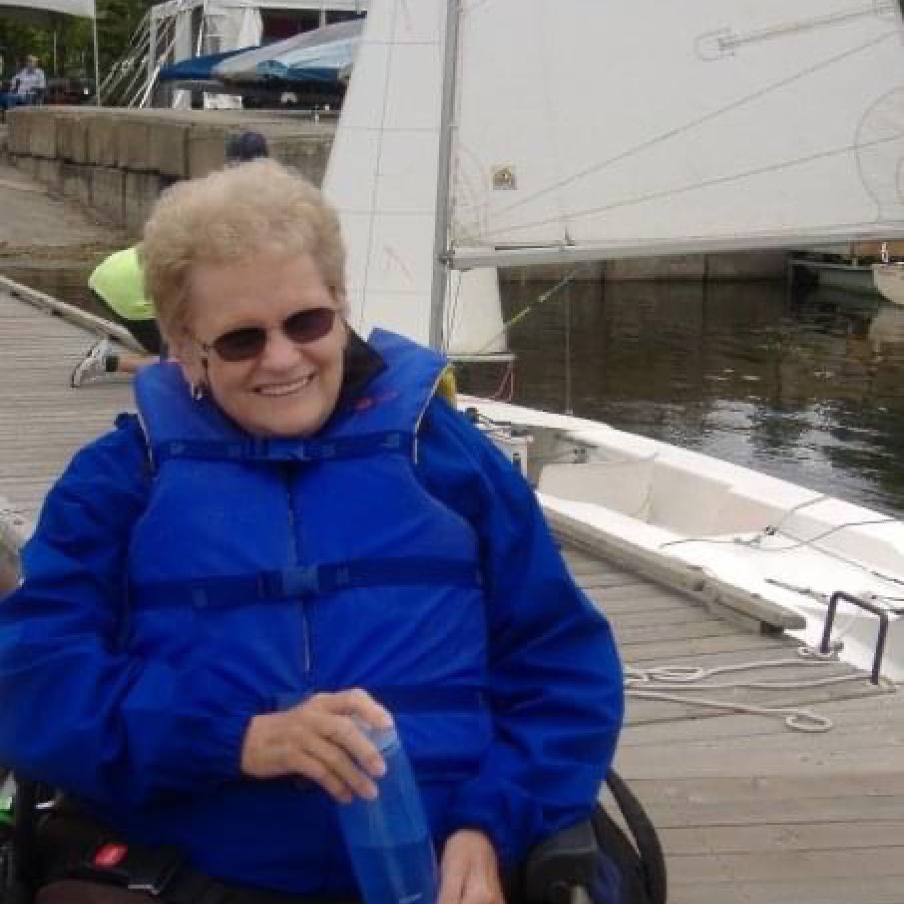 Judy Winship in her wheelchair on a dock with sailboat in background