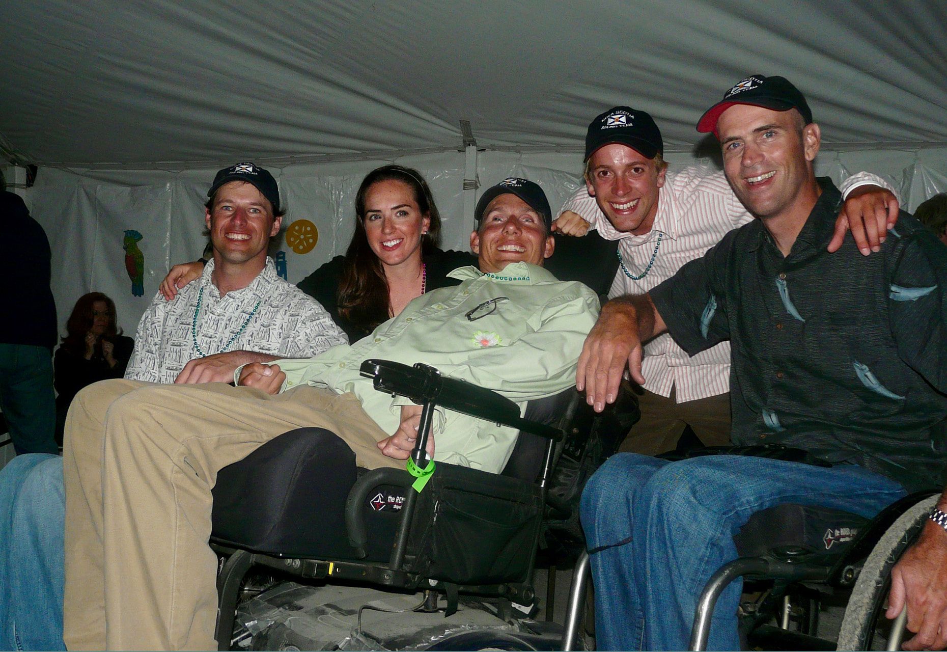 Two people in wheelchairs and three people standing n background